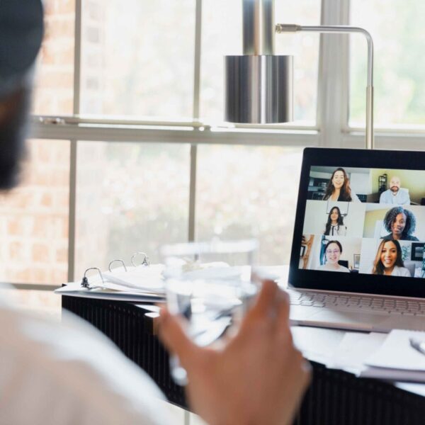 A person is sitting at their desk, looking at a screen of faces during a virtual meeting.
